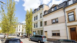 Una strada con auto parcheggiate, un furgone blu e palazzi a più piani con finestre.