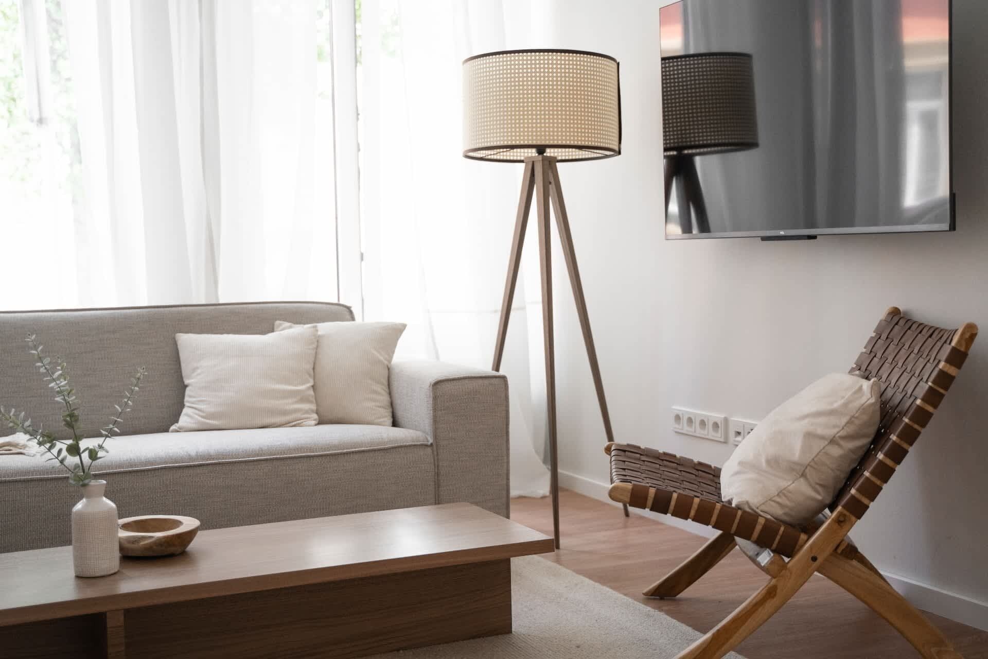 A living room with a sofa, a coffee table, a floor lamp, a TV, and a wicker chair.