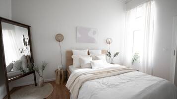 Un dormitorio con cama, mesitas de noche, espejo y ventilador de pared.