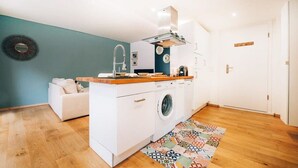 Een kleine keuken met een wasmachine, een houten aanrechtblad en een vloerkleed met een patroon.
