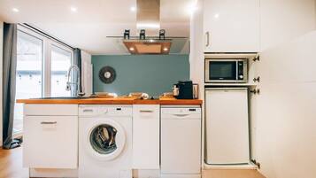 A compact kitchen with a washing machine, microwave, and a small refrigerator.