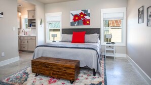 A bedroom with a bed, a bedside table, a nightstand, a window, and a painting on the wall.