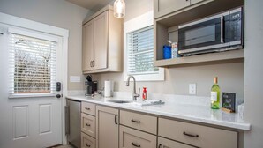 A modern kitchen with beige cabinets, a built-in microwave, and a wine bottle on the counter.