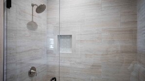 A modern shower with a glass door, a handheld showerhead, and a control panel.