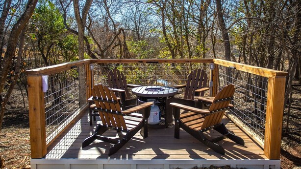 A deck with a round table and four Adirondack chairs, surrounded by a wooden fence.