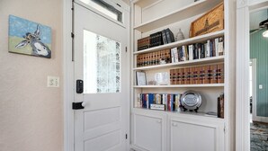 Um corredor com uma porta branca, uma estante cheia de livros e um prato decorativo na prateleira de baixo.