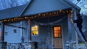 A house with a stone foundation, a wooden porch, and string lights. - The Riverfront Retreat- 27 minutes to Sugarloaf! (New Portland)