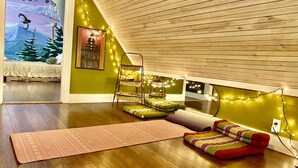 A cozy room with a sloped ceiling, wooden flooring, a bed with a green headboard, a small sofa, and a yoga mat. - The Riverfront Retreat- 27 minutes to Sugarloaf! (New Portland)