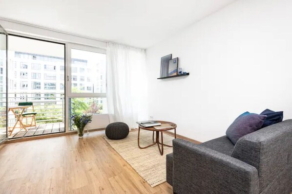 Una sala de estar moderna con un sofá gris, una mesita redonda y un amplio ventanal con vistas a la ciudad.