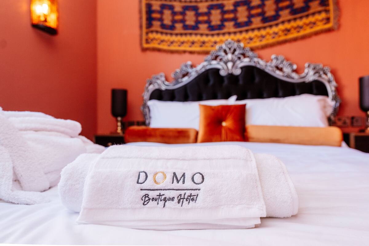 Un lit parfaitement fait, avec des serviettes blanches pliées, et une pancarte indiquant « DOMO Boutique Hotel ».