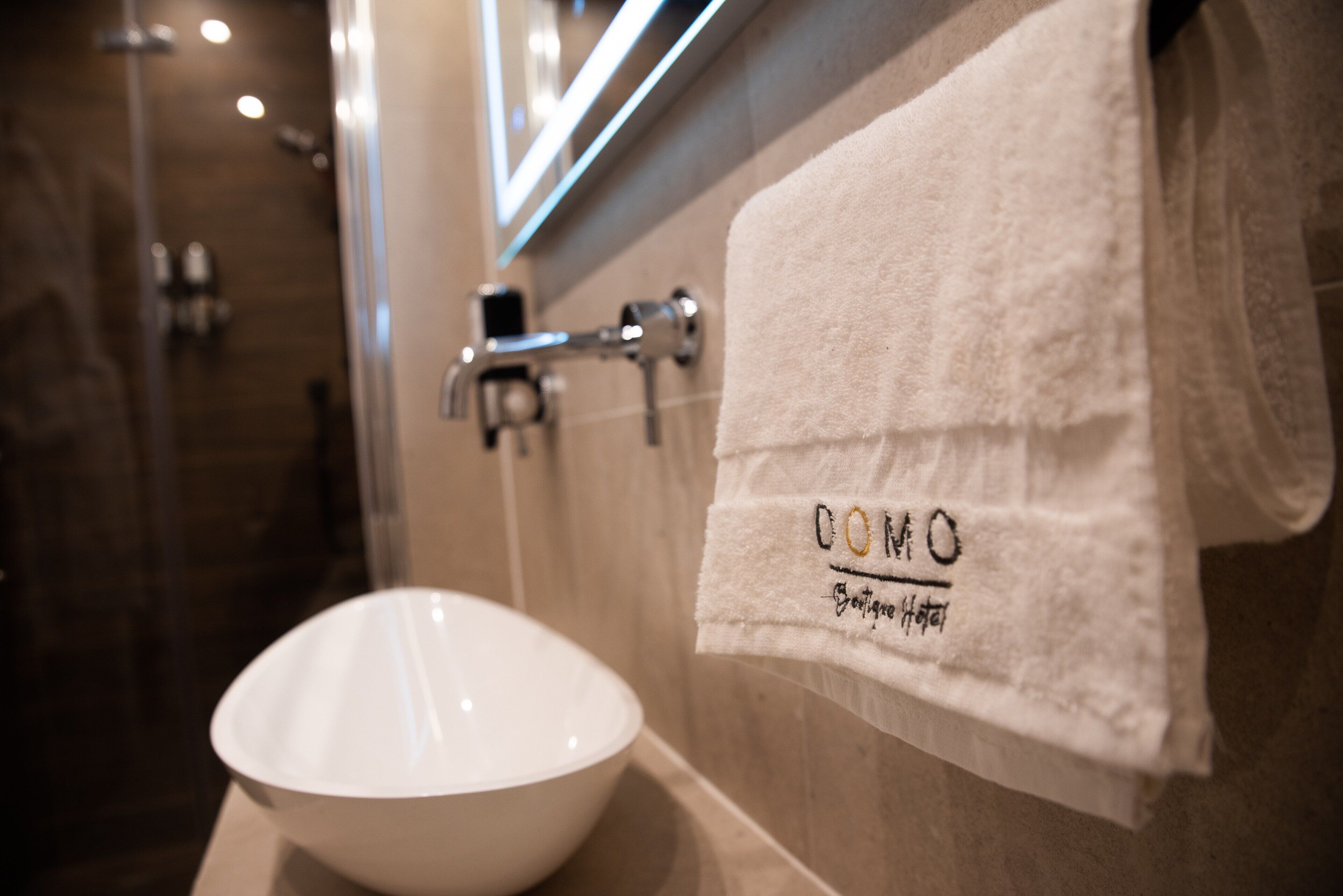 Um banheiro com uma pia branca e uma toalha pendurada na parede, com a inscrição 'COMO' e 'Hotel'.