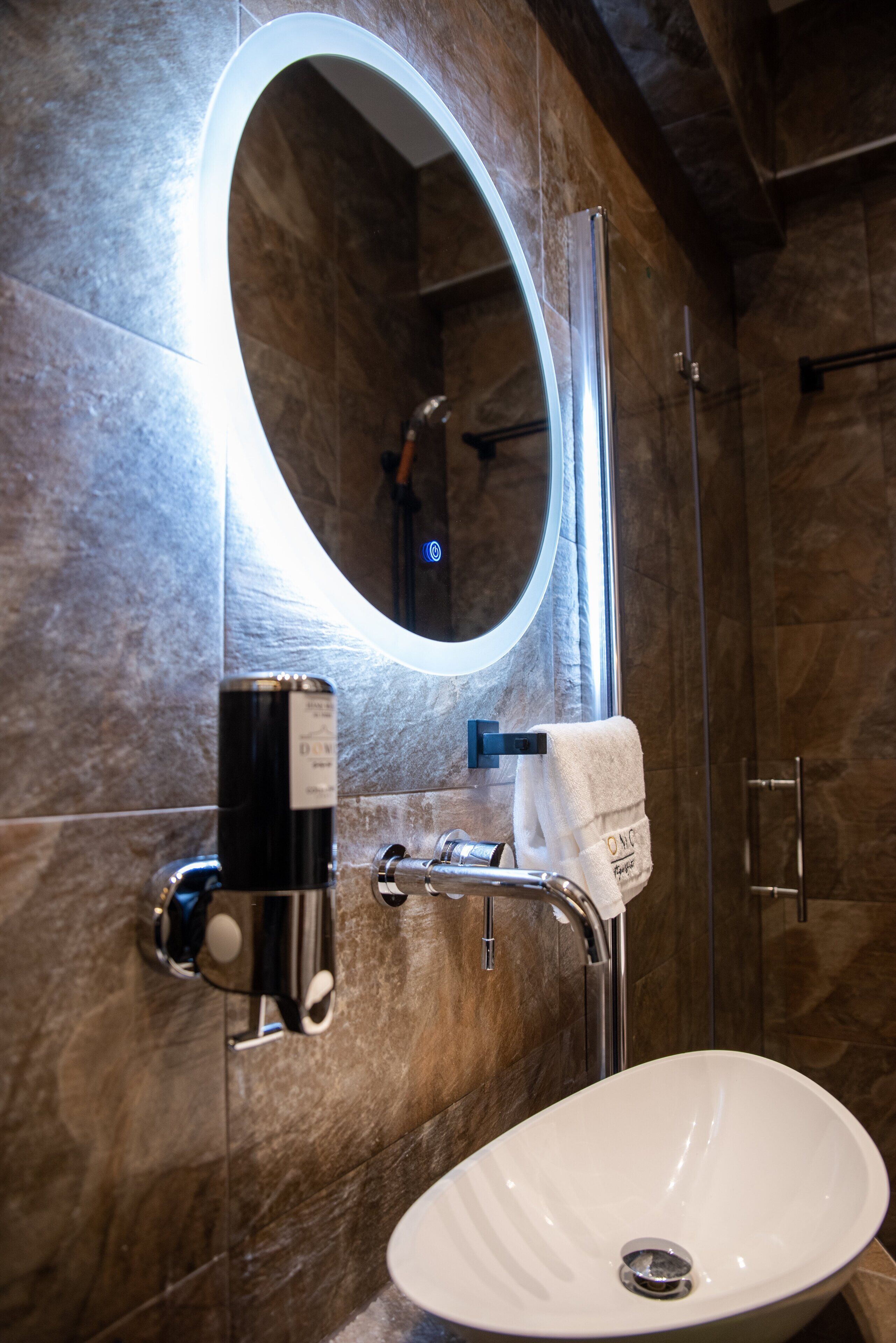 Une salle de bain avec un lavabo blanc, un miroir avec un éclairage intégré et un porte-serviettes.