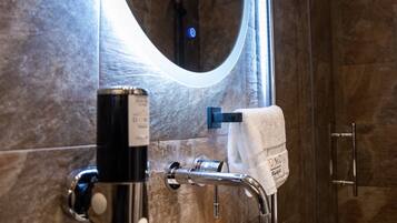 Une salle de bain avec un lavabo blanc, un miroir avec un éclairage intégré et un porte-serviettes.