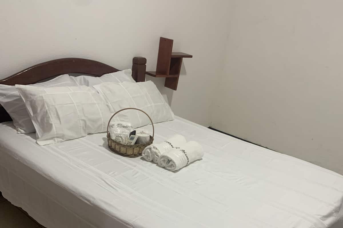 A neatly made bed with white linens, a small bedside table with a lamp, and a basket with toiletries.