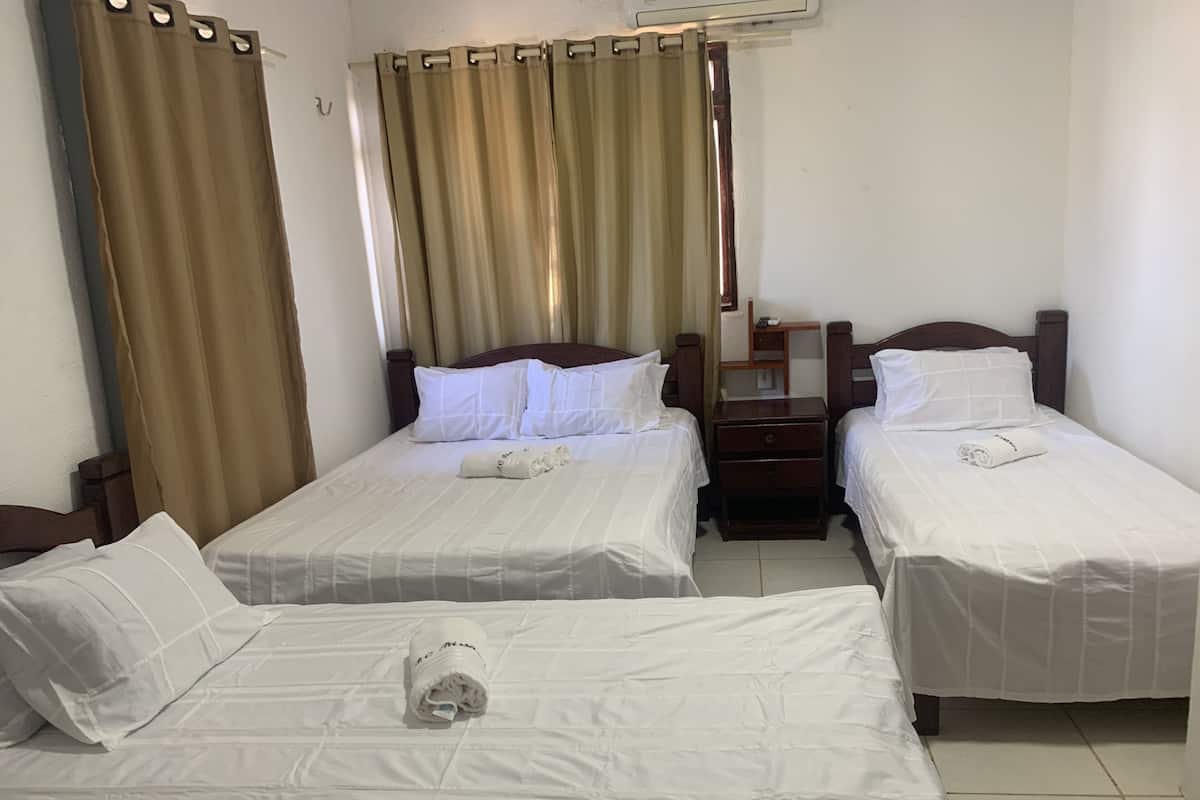 A hotel room with two single beds, a wooden nightstand, a small table, and a window with curtains.