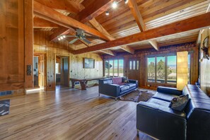 Un salon spacieux doté de planchers en bois, d’un ventilateur de plafond et de grandes fenêtres offrant une vue sur l’extérieur.