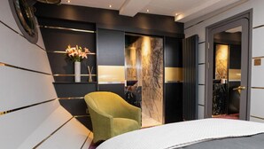 A modern bedroom with a bed, a green armchair, a marble wall, and a door leading to another room.