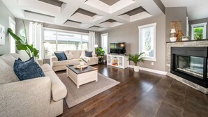 A spacious living room with a large TV, comfortable seating, a fireplace, and a view of the outdoors. - Amazing Luxe Home w/ AirCon & HUGE Yard | FirePit (Edmonton)