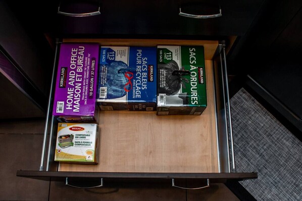 A drawer with various items including a purple box labeled 'Home and Office Maison Et Bureau', a blue box labeled 'Sacs Bleus', a green box labeled 'Sacs A Cordures', and a white box labeled 'BioSak'. - Amazing Luxe Home w/ AirCon & HUGE Yard | FirePit (Edmonton)
