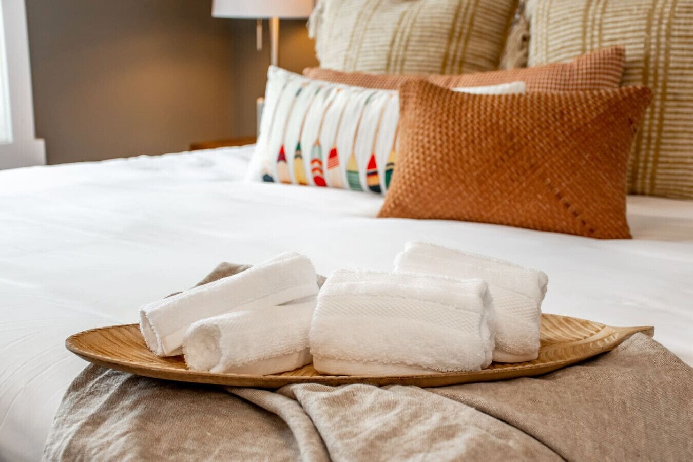 Un lit bien fait, avec du linge de lit blanc, un plateau en bois sur lequel sont pliées des serviettes, et une variété d'oreillers en arrière-plan.