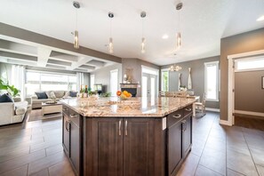 A spacious kitchen with a large island, dark wood cabinetry, and pendant lighting. - Amazing Luxe Home w/ AirCon & HUGE Yard | FirePit (Edmonton)