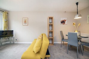 Un salon comprenant un canapé, un téléviseur, une table à manger avec des chaises et une bibliothèque.