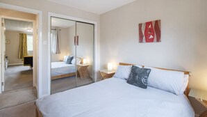 Une chambre à coucher comprenant un lit, des tables de chevet, un miroir et une porte donnant sur une autre pièce.