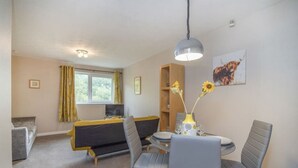 Une pièce comprenant un lit, une table à manger avec des chaises, un vase de fleurs et un tableau accroché au mur.
