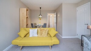 Un canapé jaune dans un salon, avec une table à manger et des chaises en arrière-plan.