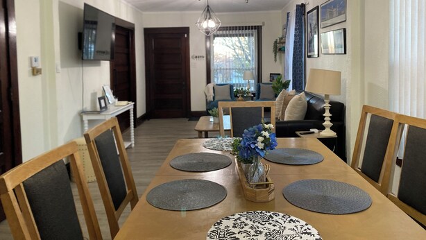 Un comedor con una mesa de madera, individuales grises y un jarrón con flores.