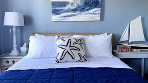 Un dormitorio con una cama, un cojín con forma de estrella de mar, un modelo de velero y una pintura de una ola.