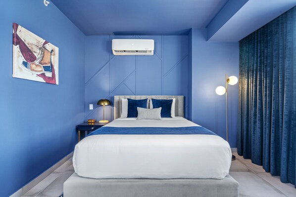 A modern bedroom with a large bed, a wall-mounted air conditioner, a floor lamp, and a painting on the wall. - Don Rafa Boutique Hotel & Residences (San Juan)