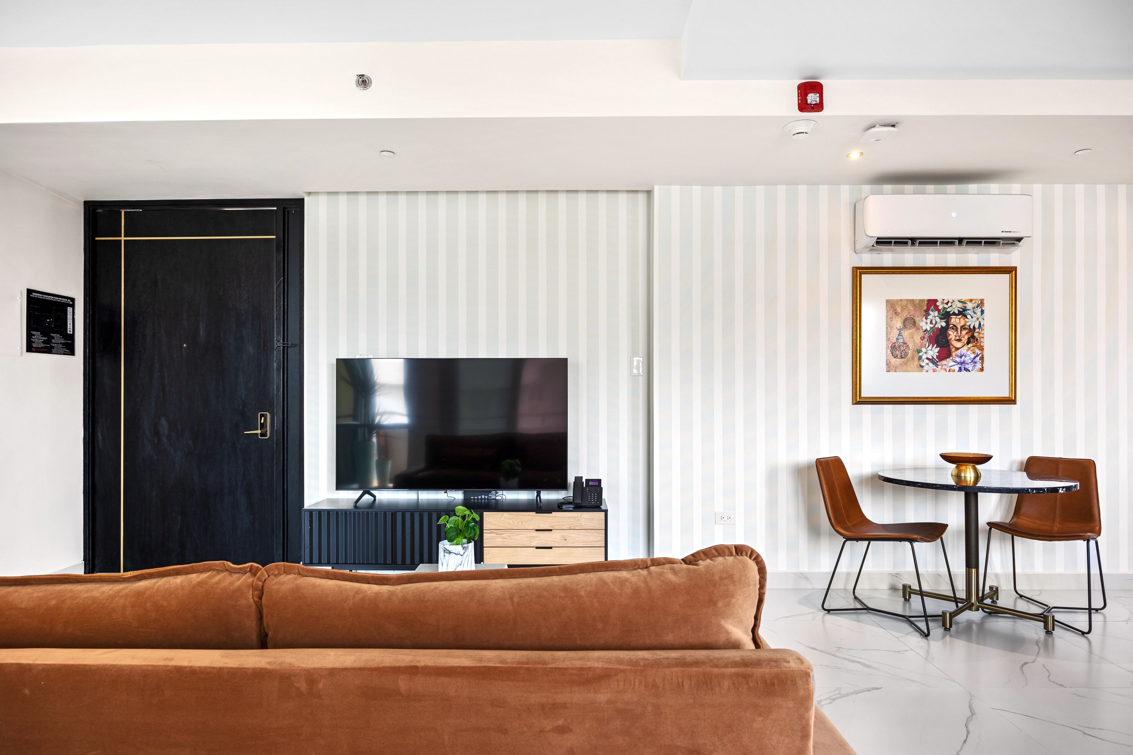 A modern living room with a brown sofa, a flat-screen TV, a dining area with two chairs and a small table, and a black door.