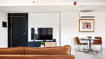 A modern living room with a brown sofa, a flat-screen TV, a dining area with two chairs and a small table, and a black door.
