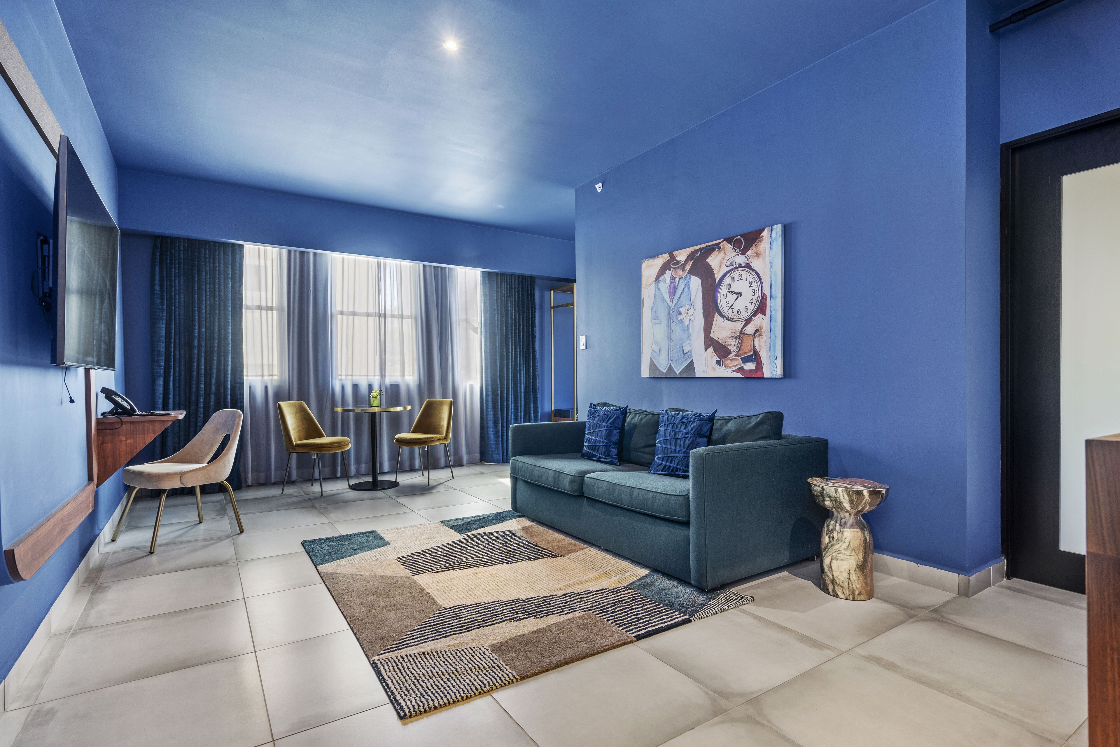 A modern living room with a blue accent wall, a sofa, two chairs, a coffee table, and a large painting.