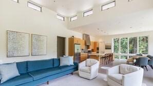 Un salón amplio con un sofá azul, sillones blancos y una cocina al fondo.