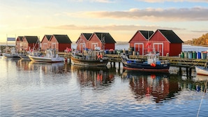 A waterfront scene with red wooden houses and boats docked at a pier. - Baltischer Hof, Apartment 20 (Boltenhagen)