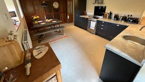 A modern kitchen with dark cabinetry, a built-in oven, and a large island with a sink. - Braunston Manor Cottage: 4-poster beds & ensuites (Braunston)