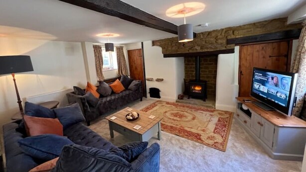 A cozy living room with a sofa, a coffee table, a fireplace, and a television. - Braunston Manor Cottage: 4-poster beds & ensuites (Braunston)
