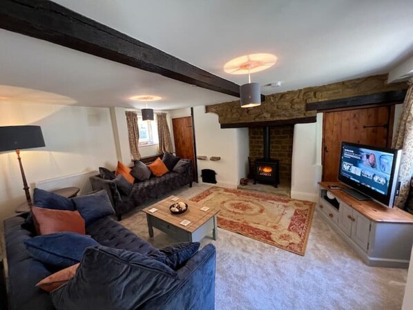 A cozy living room with a sofa, a coffee table, a fireplace, and a television. - Braunston Manor Cottage: 4-poster beds & ensuites (Braunston)