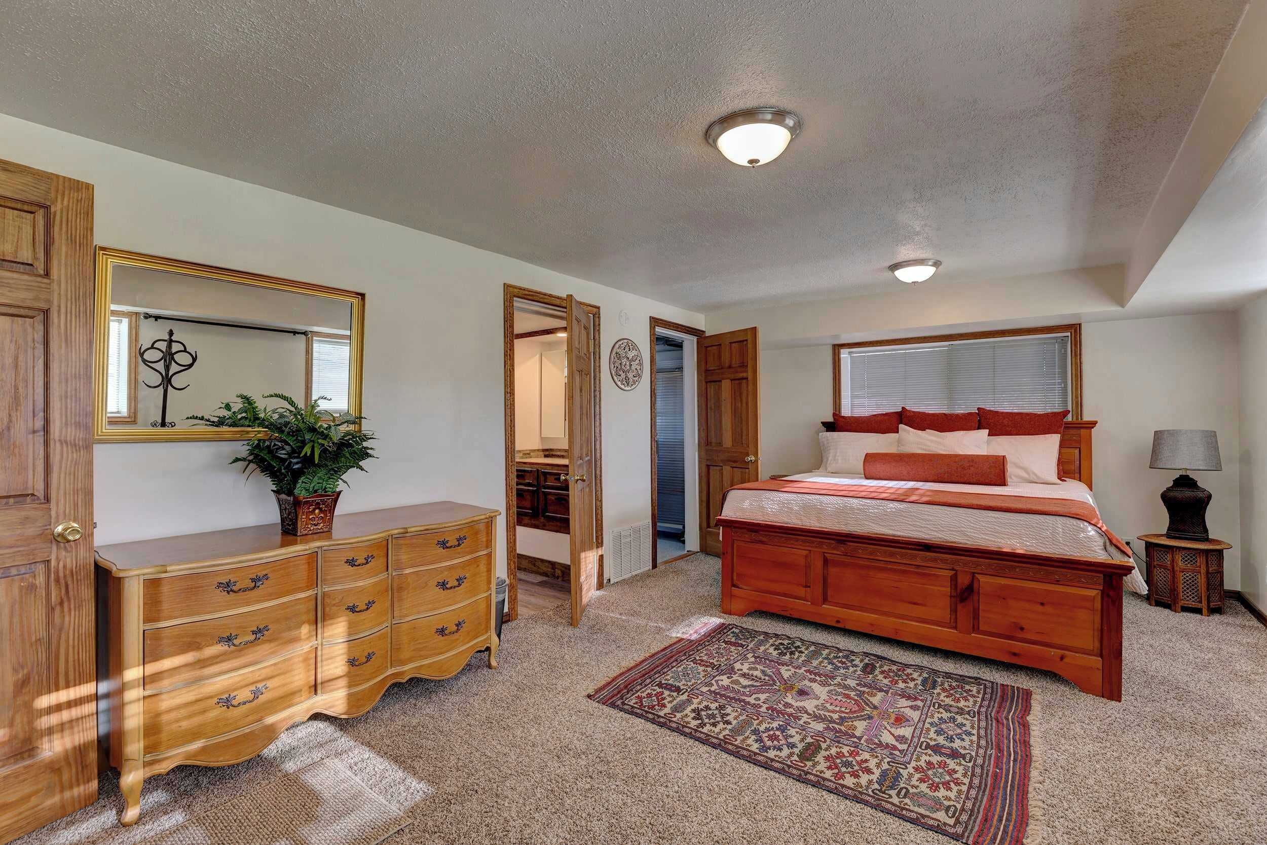 A bedroom with a wooden bed, a dresser, a mirror, and a carpeted floor.