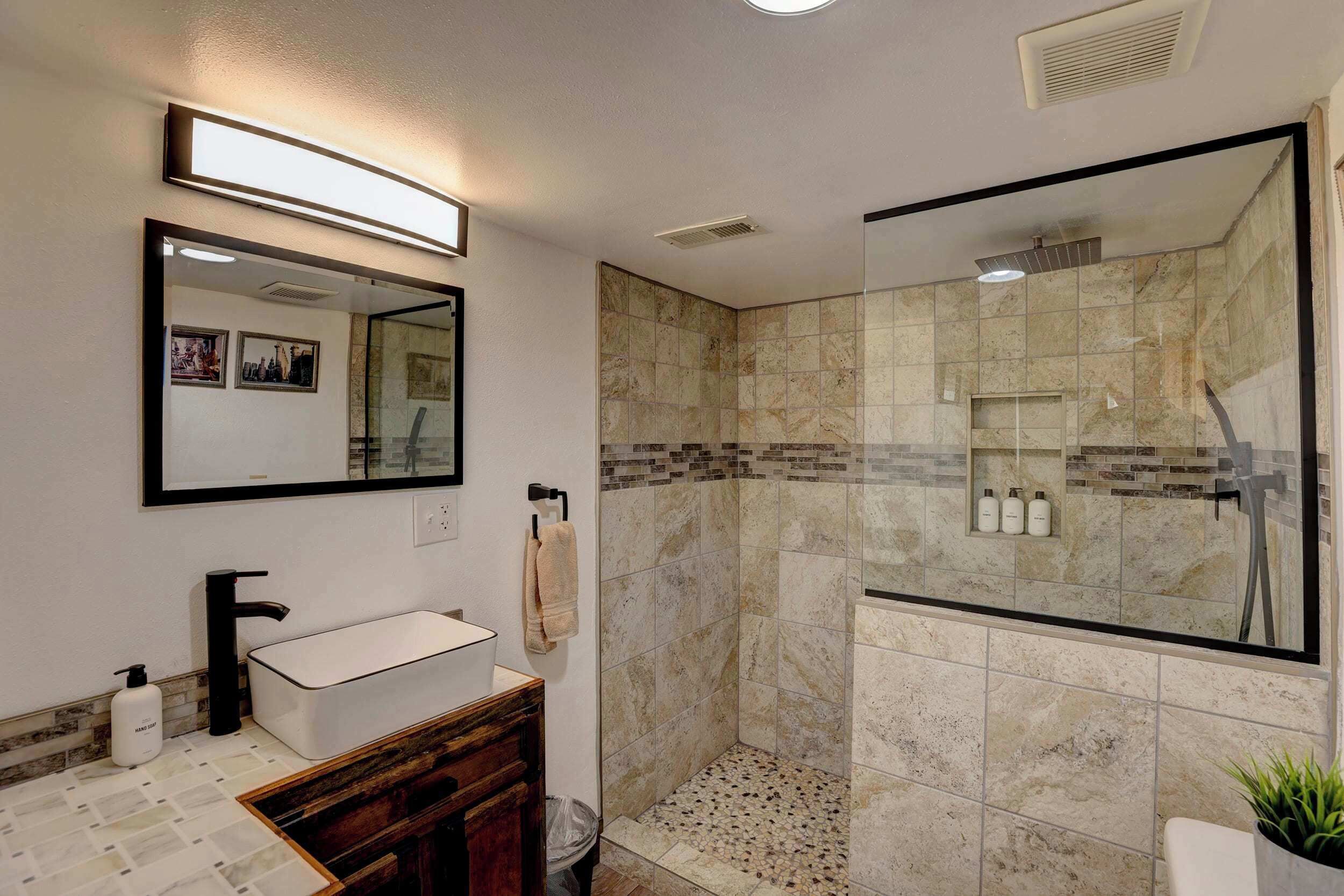 Un baño moderno con un lavabo blanco, cabina de ducha con mampara de vidrio y espejo sobre el lavabo.
