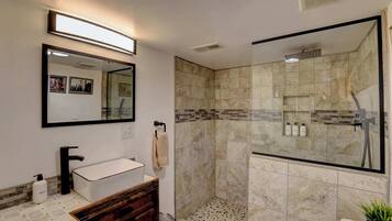 Un baño moderno con un lavabo blanco, cabina de ducha con mampara de vidrio y espejo sobre el lavabo.