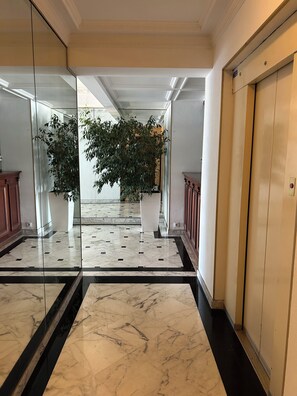Um corredor com piso de mármore, uma planta em vaso e uma porta de madeira.