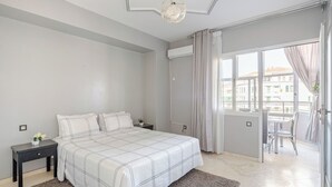 Un dormitorio con una cama grande, una mesita de noche, una pequeña mesa con una planta y vistas al exterior a través de una puerta corrediza.