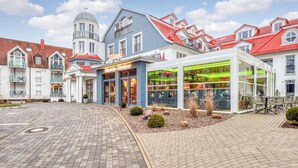 Ein modernes Hotel mit einer zentralen Glasfassade, einem Innenhof mit Backsteinpflasterung und traditioneller europäischer Architektur im Hintergrund.