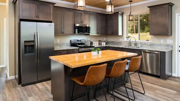 Una cocina moderna con armarios oscuros, electrodomésticos de acero inoxidable y una isla de madera con taburetes de bar.