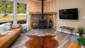 Una sala de estar acogedora con chimenea de piedra, un sofá cómodo, un televisor de pantalla plana y un ventanal con vistas al exterior.