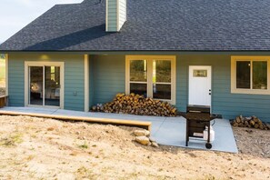 Ein Haus mit überdachter Terrasse, Grill und Holzstapel.