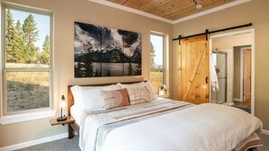 Un dormitorio con una cama grande, un cuadro de montañas, una puerta corredera y vistas a árboles.